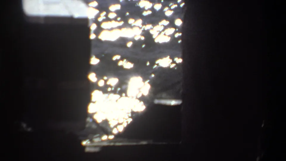 Cropped 8mm frame from Khartoum showing a dark foreground figure, boat structure, and sunlit water beyond.