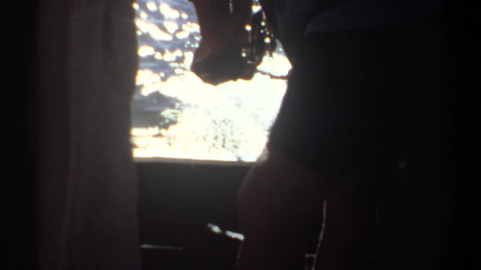 1969 Khartoum home-movie frame with cropped people at a boat edge and bright reflected water filling the background.