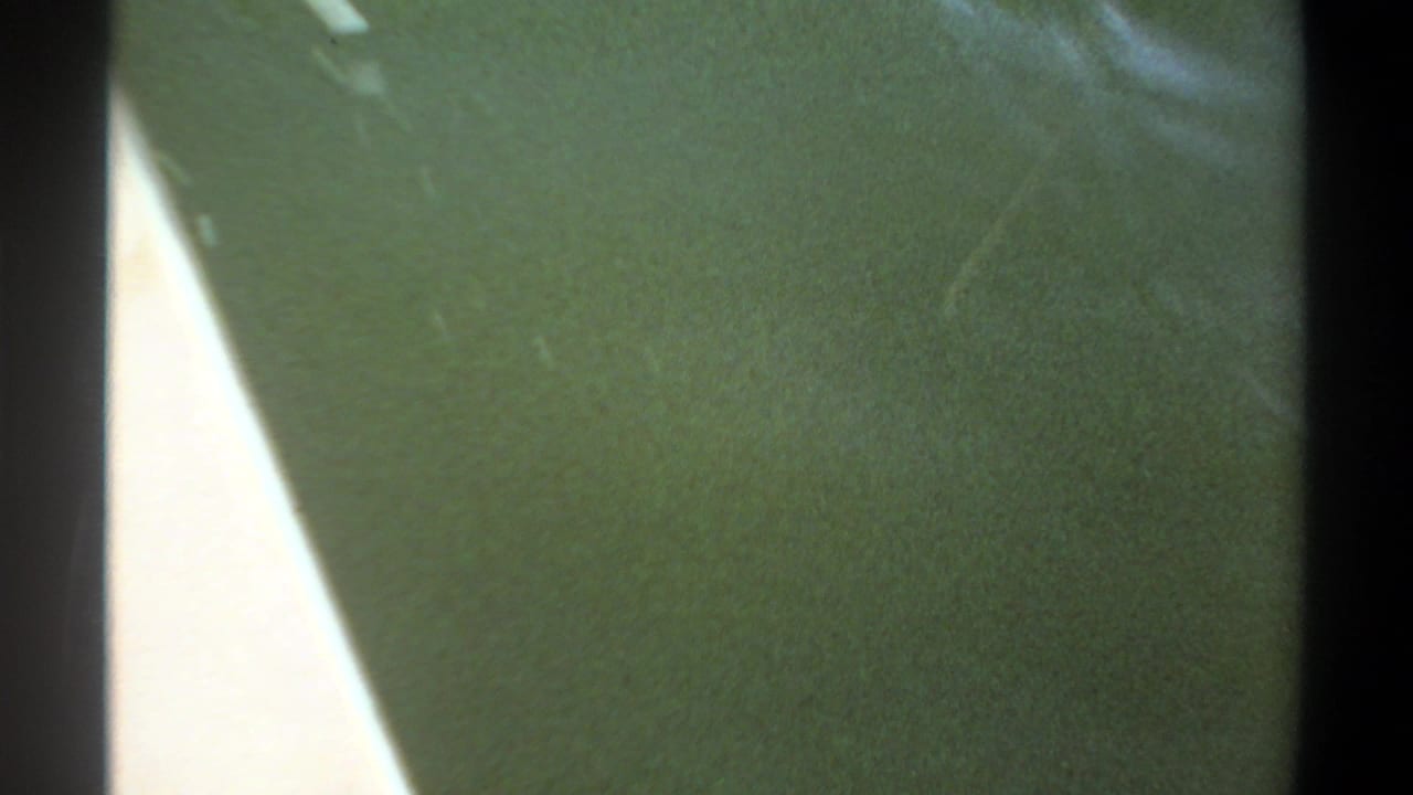 1969 Khartoum home-movie frame showing murky green water, dark gate edges, soft grain, and a bright triangular overexposed area at left.