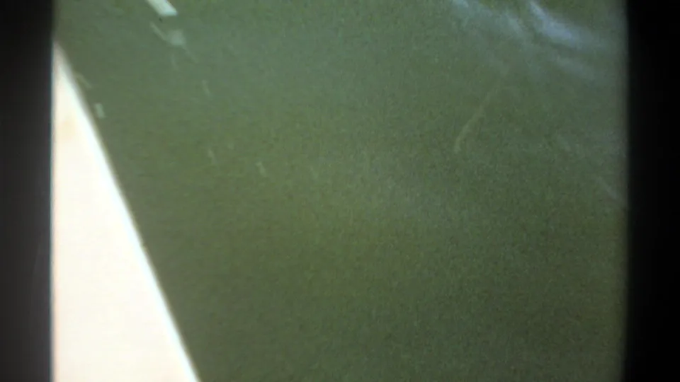 1969 Khartoum home-movie frame showing murky green water, dark gate edges, soft grain, and a bright triangular overexposed area at left.