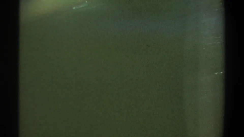 1969 Khartoum home-movie frame with dark green water, black vertical gate edges, faint surface texture, and visible 8mm grain.