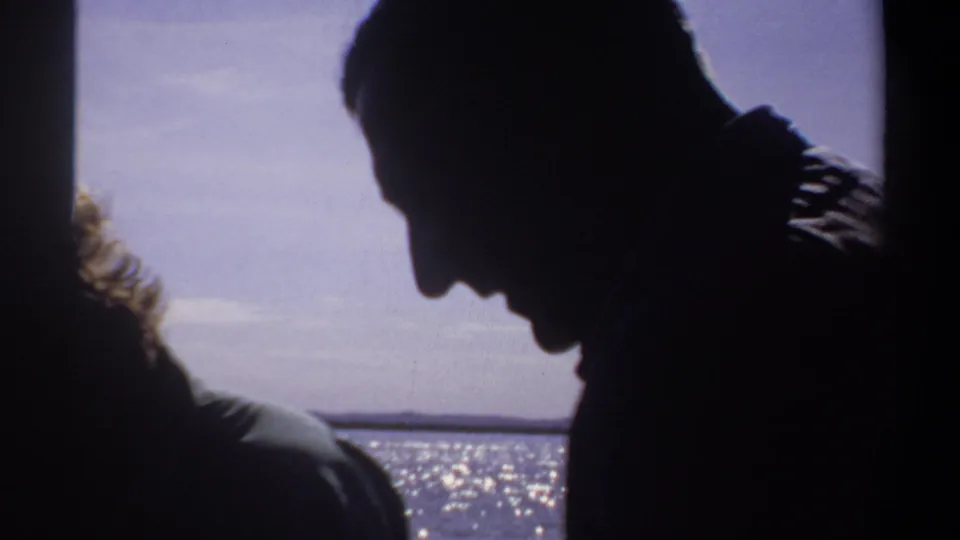 A dark silhouetted passenger is framed against sparkling water and distant shore, continuing the Khartoum, Sudan boat scene.