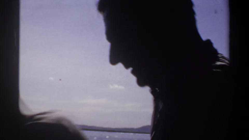 A silhouetted adult profile appears beside a boat window, with shimmering water and sky outside in Sudan footage from 1969.