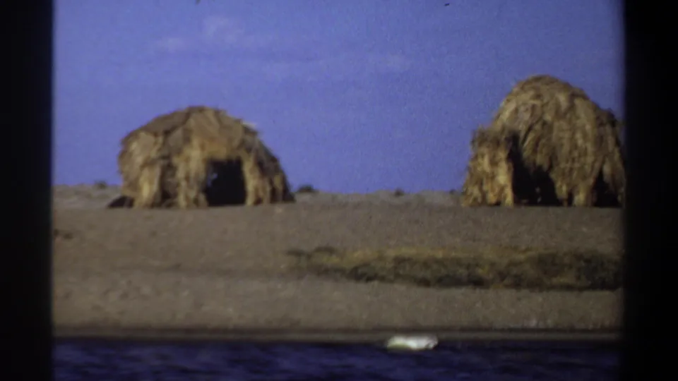 Two straw-covered huts stand on dry terrain in a 1969 Khartoum-area home-movie frame.