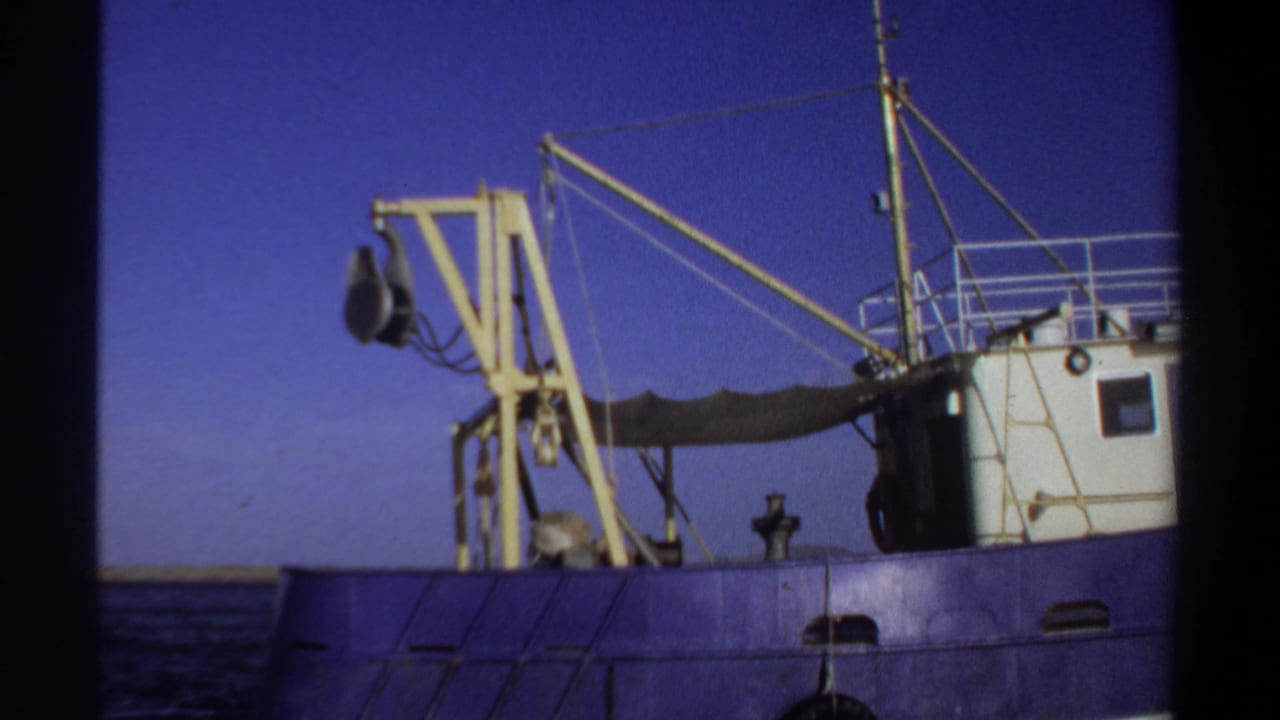 Blue boat hull with yellow crane and white cabin seen across open water.