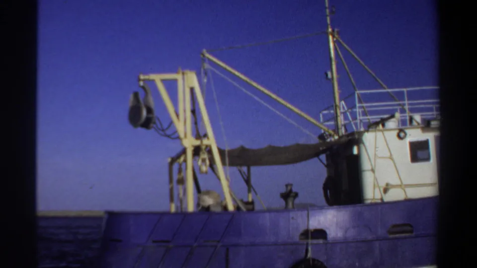 1969 Sudan-listed 8mm frame showing a blue working boat with a yellow crane, white cabin, rigging, and dark sea under a clear sky.