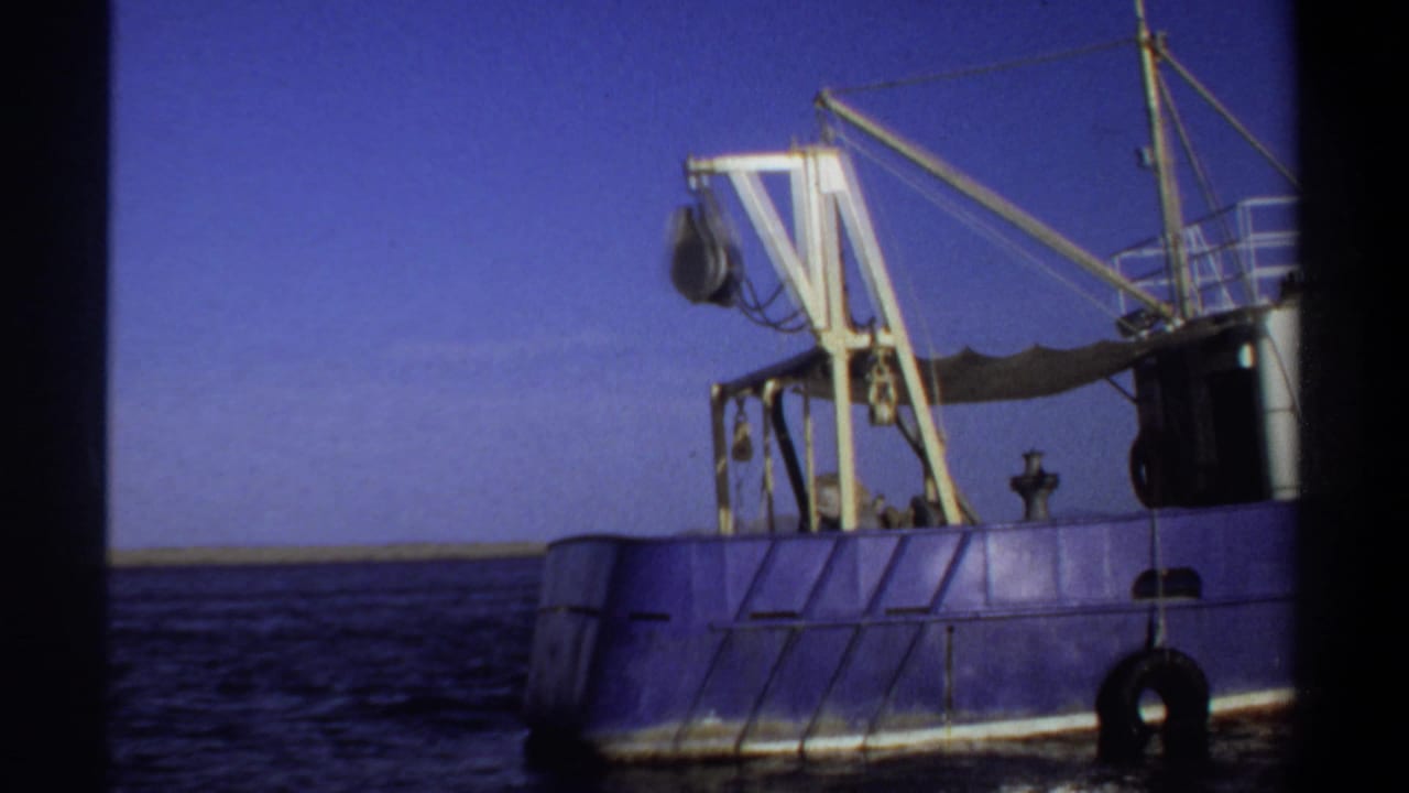 Side of a blue vessel with yellow crane, rigging, and sea horizon.