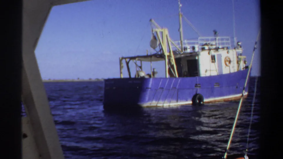1969 Sudan-listed frame showing more of the blue working boat, including its white cabin, yellow crane, hanging tires, rigging lines, and water surface.
