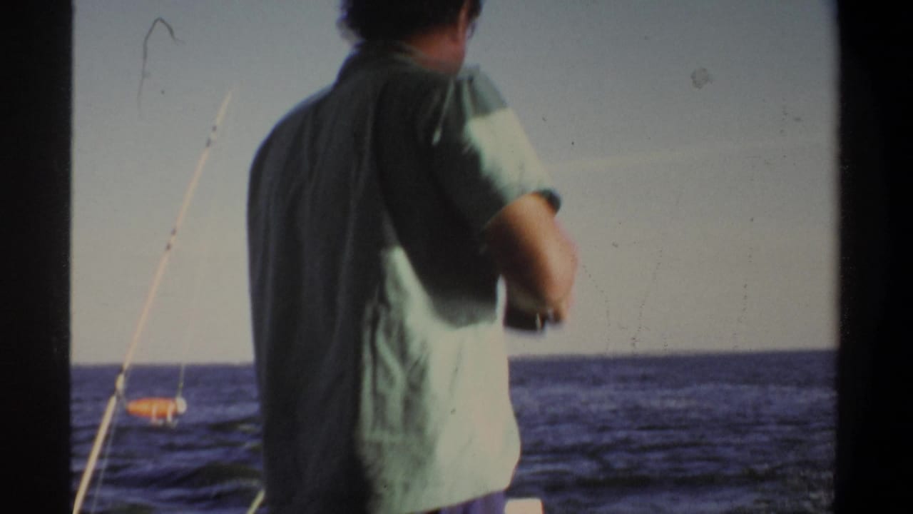 Adult man in a light green shirt stands on a boat, seen from behind against open water in 1969 home-movie footage from Sudan metadata.