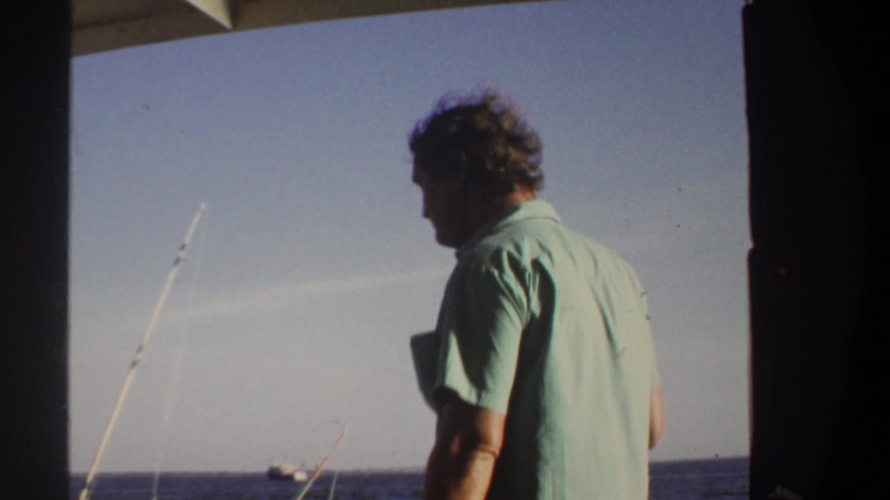 Side profile of an adult man holding a bottle on a boat, with fishing rods, blue water, and bright sky visible.