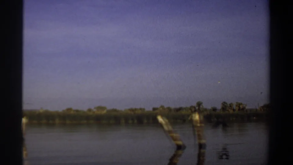 1969 Khartoum river cutaway showing angled wooden posts, smooth water, distant trees, and muted 8mm color.
