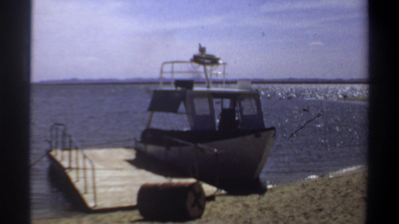 Cabin powerboat by the shore with water and distant land behind it.