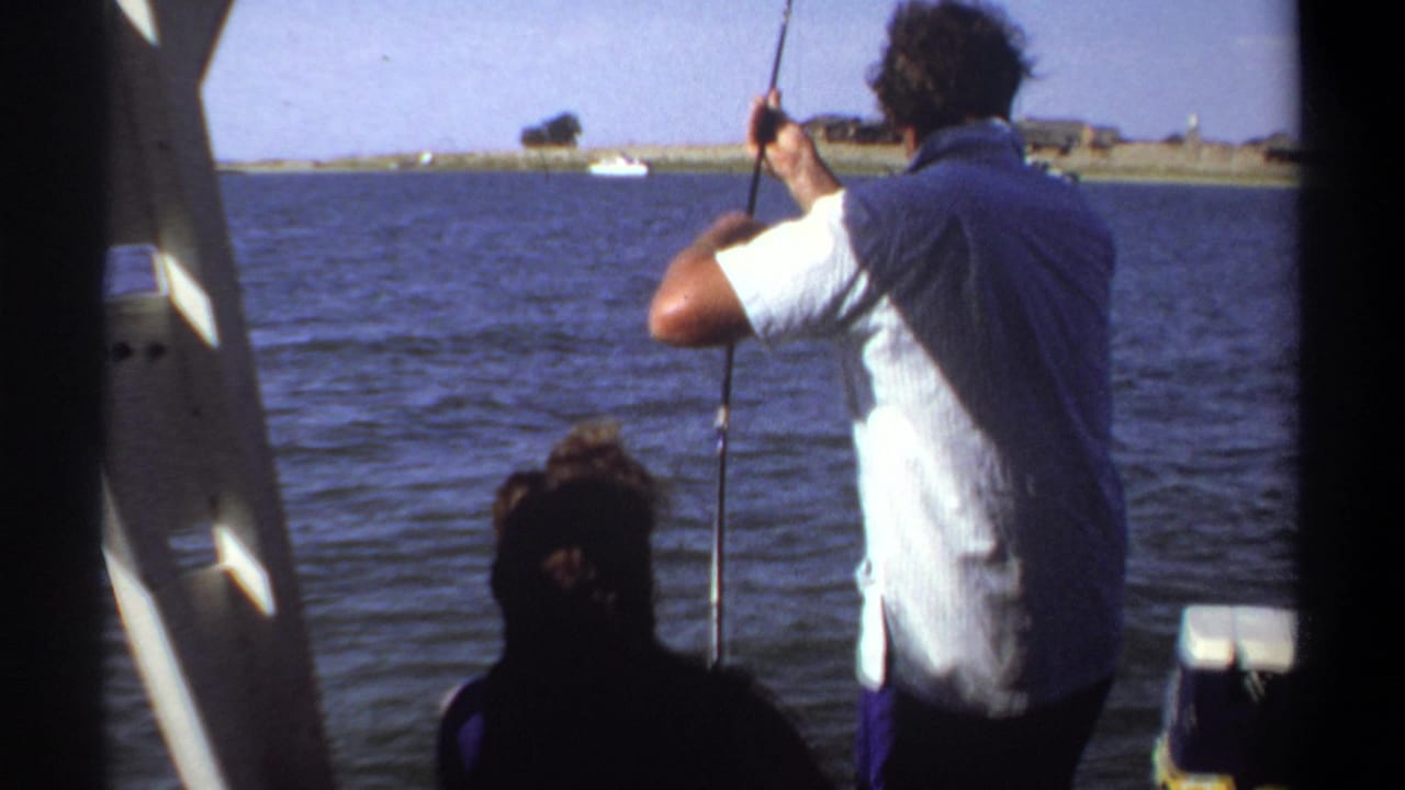 Standing angler holds a fishing rod at the side of a boat with a silhouetted companion nearby.