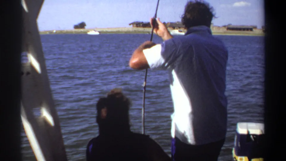 1969 Khartoum 8mm frame showing the man fishing from the boat, with a companion low in frame and small boats near the shore.