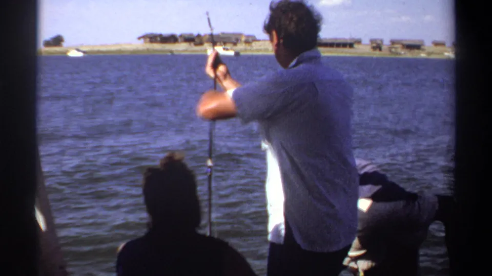 1969 Khartoum lake footage frame showing a standing fisherman, seated passenger, and another person leaning near the boat edge.