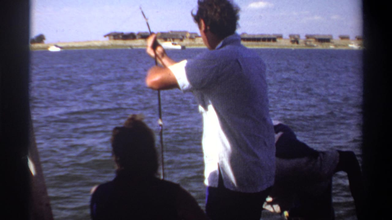 Man in a light shirt casts a fishing pole from a small boat on open water.