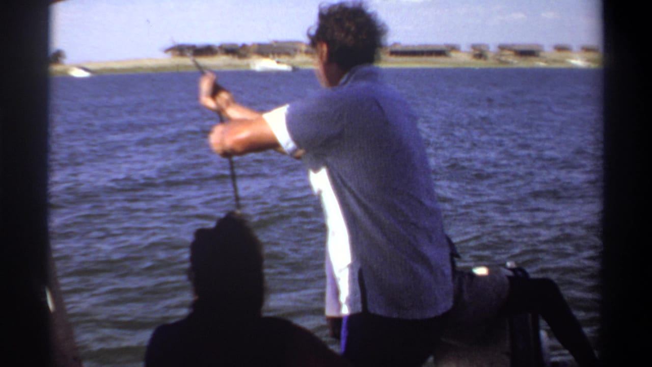 1969 Khartoum frame with a man working a fishing pole from a small boat as rippled water and a low shoreline fill the background.