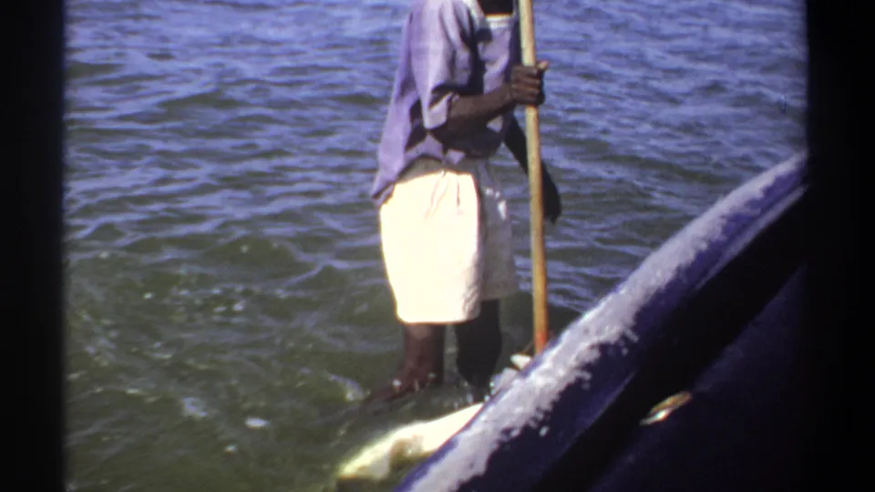 1969 Khartoum home-movie frame showing a man wading near the boat with a long pole, partly cropped by the handheld camera.