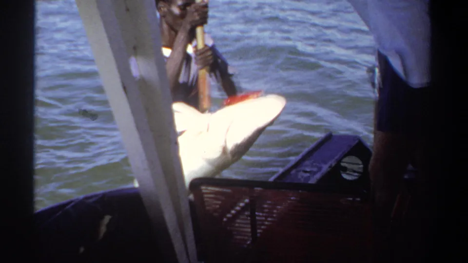 1969 Khartoum footage frame showing a man near the boat handling a large pale fish with a pole on sunlit water.