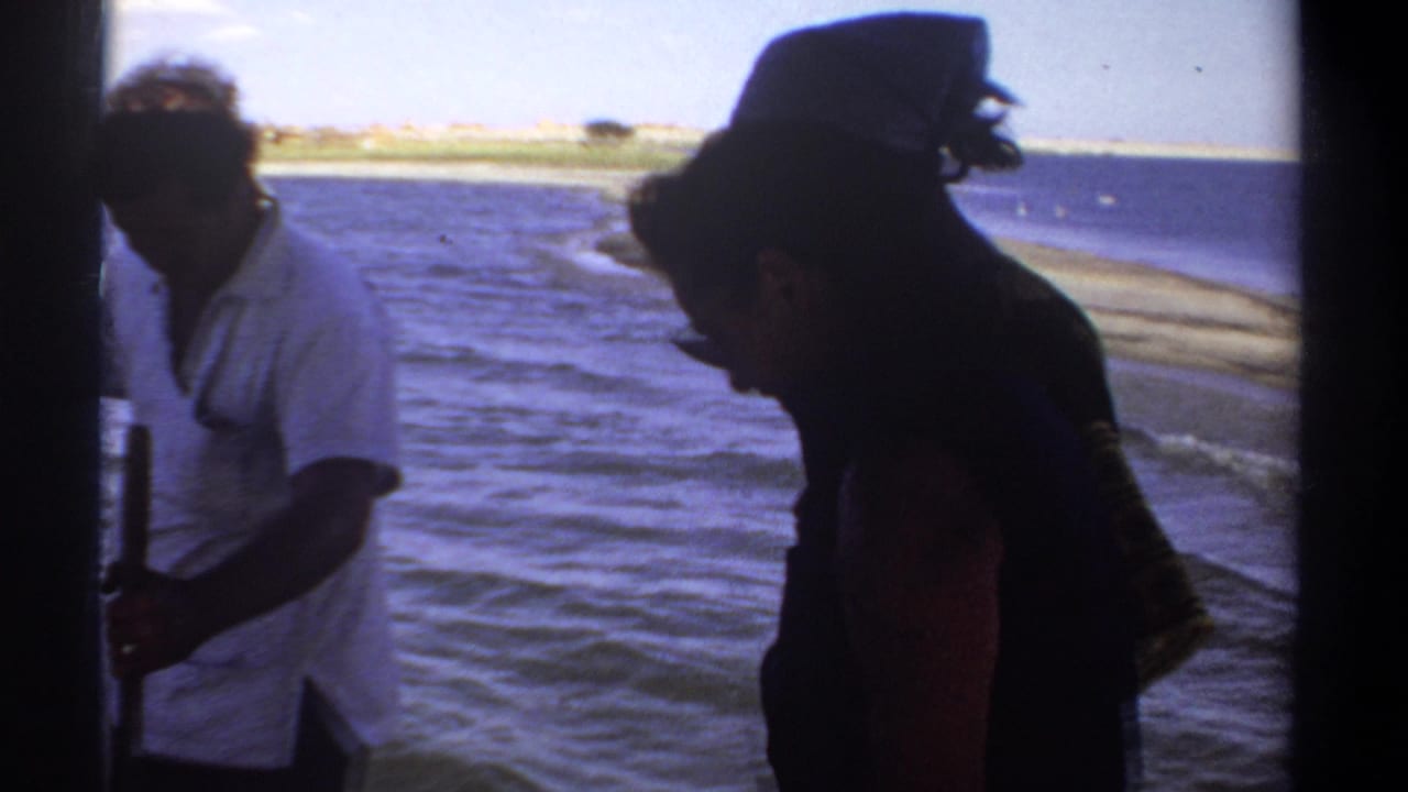 A man in a light shirt and a woman in dark clothing appear aboard a boat near a distant shoreline in 1969 Sudan footage.