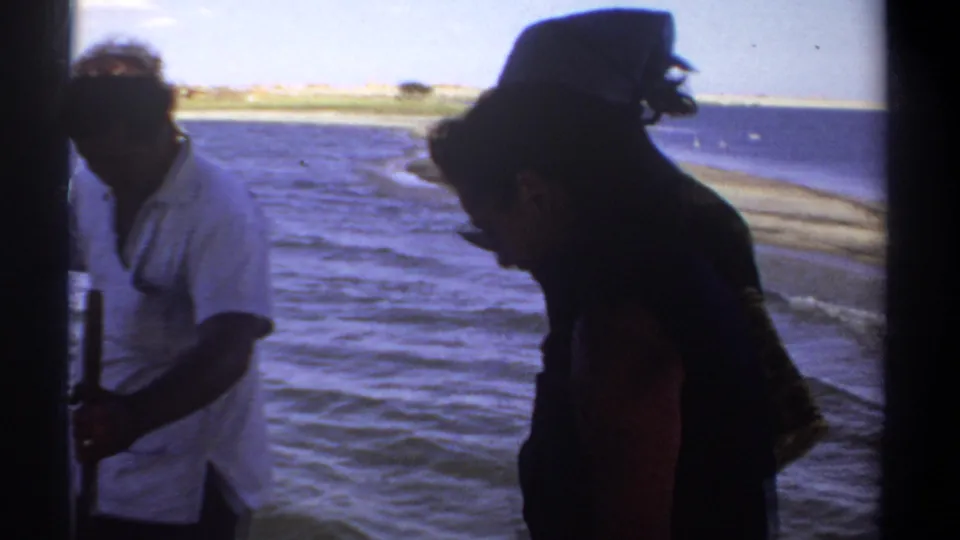 A man in a light shirt and a woman in dark clothing appear aboard a boat near a distant shoreline in 1969 Sudan footage.