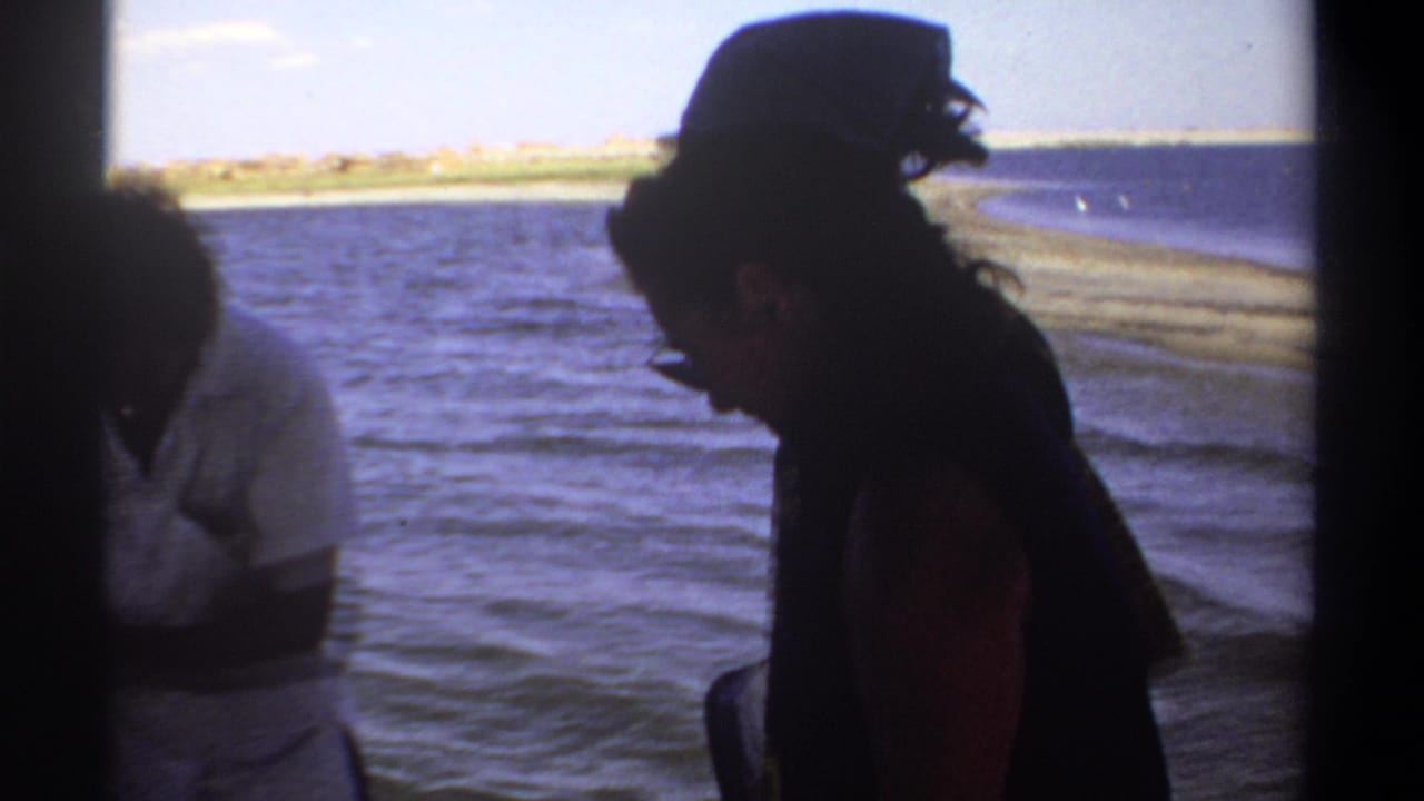 1969 Khartoum home-movie frame showing adults on a boat by open water, one figure partly silhouetted in strong sun.