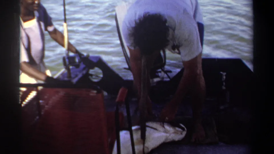 The Khartoum 1969 home movie shows an adult handling a large fish on a small boat deck with open water behind.
