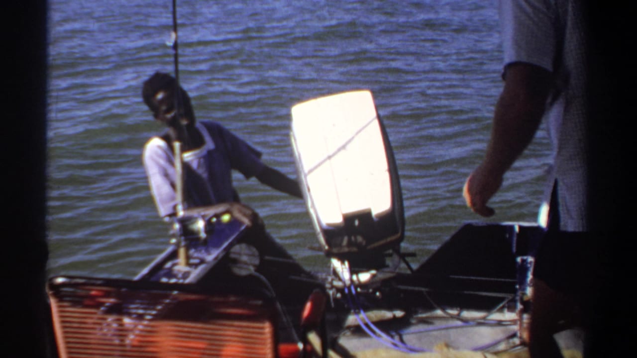 Two men near a small motorboat on calm water, with dark film-frame edges.