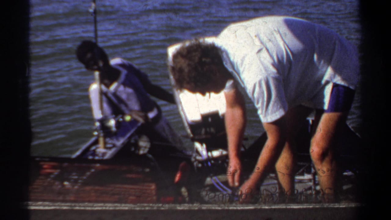 1969 Khartoum travel footage frame with a man leaning into a small motorboat and another person seated near the water.