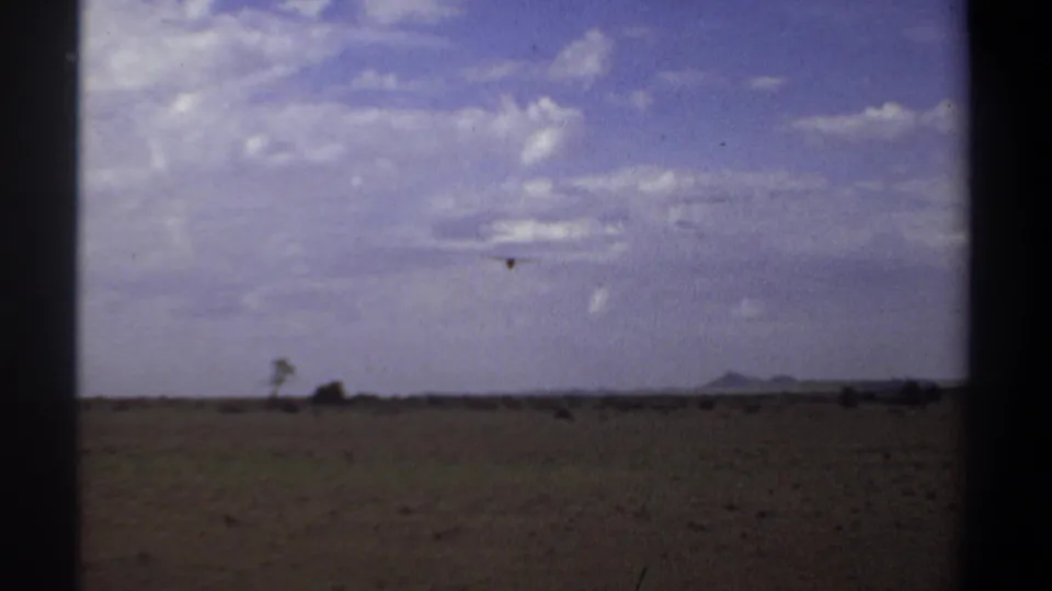 1969 Sudan home-movie frame of an arid field and broad sky, with a small bird faintly visible above the distant horizon.