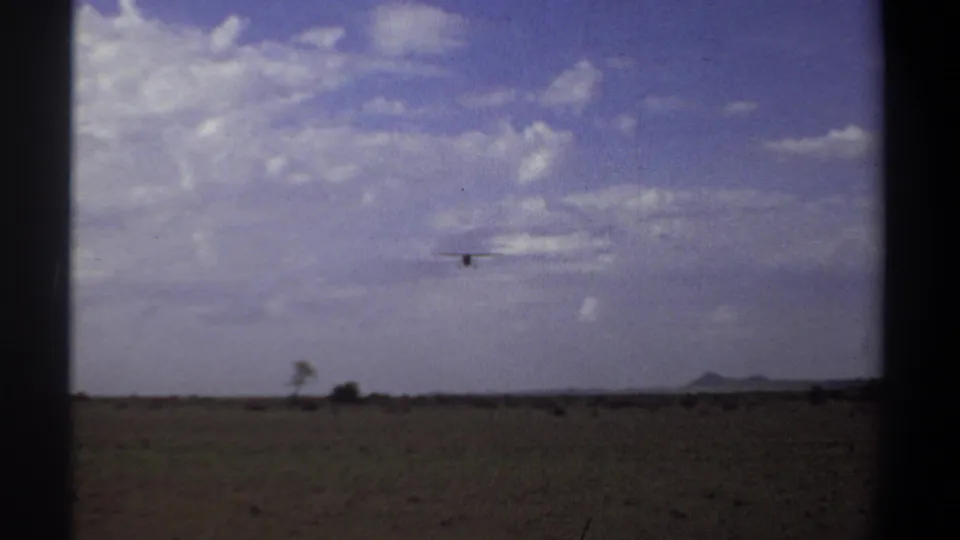 Final 1969 Khartoum frame with a small bird above open countryside, scattered clouds, distant low hills, and visible 8mm frame edges.