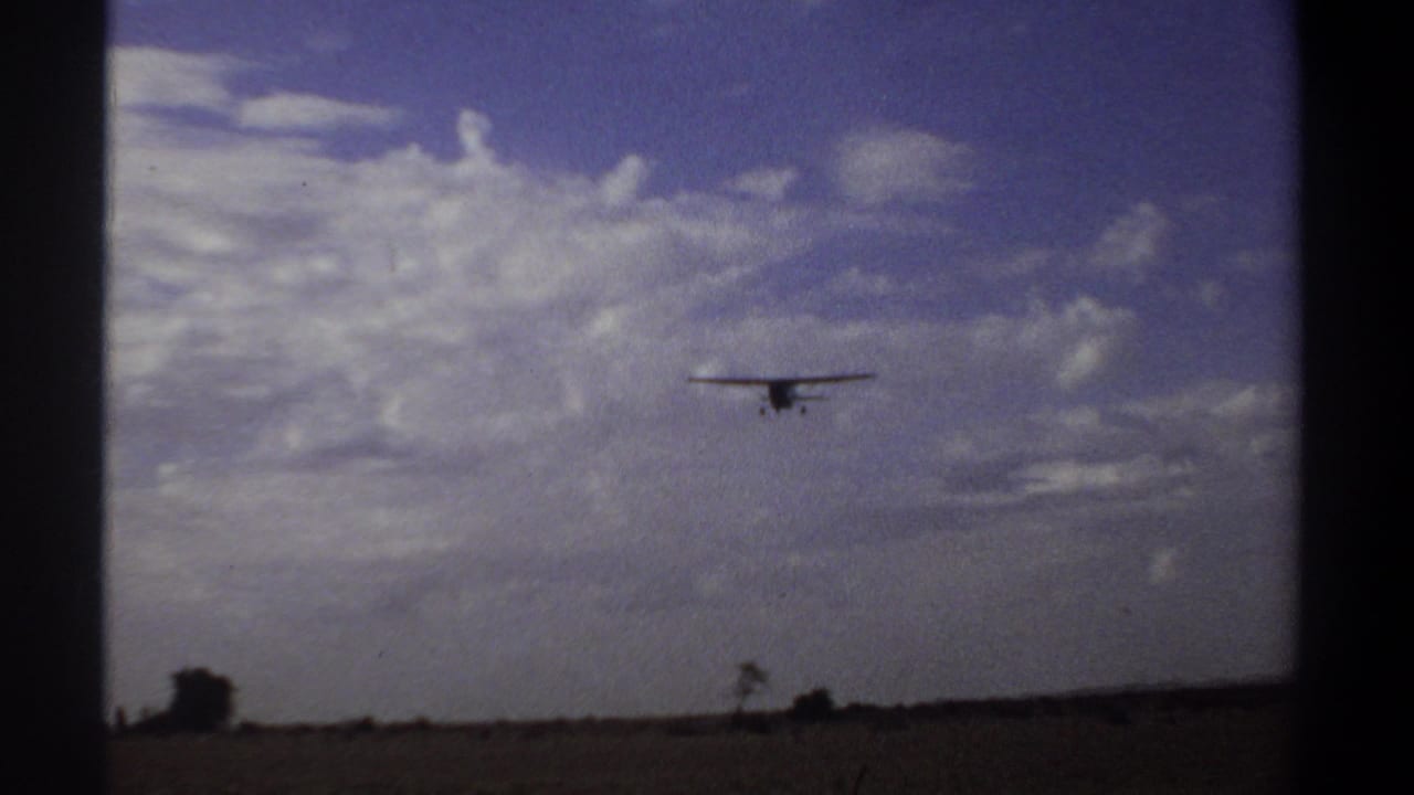 Small airplane flying low above a sparse horizon with clouds behind it.