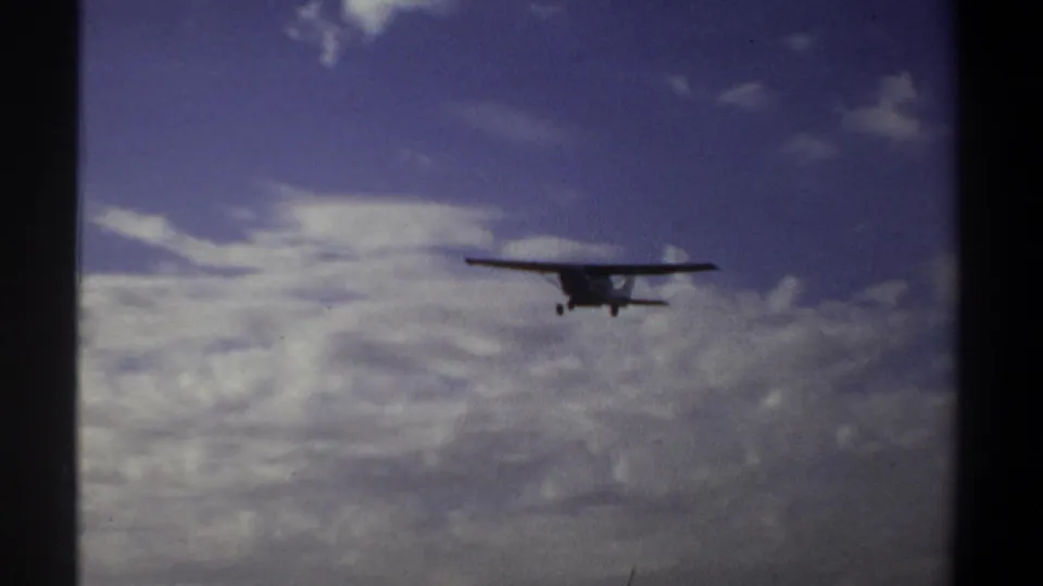 Closer 8mm view of a small propeller aircraft flying toward the camera above Khartoum, Sudan, with clouds filling the background.