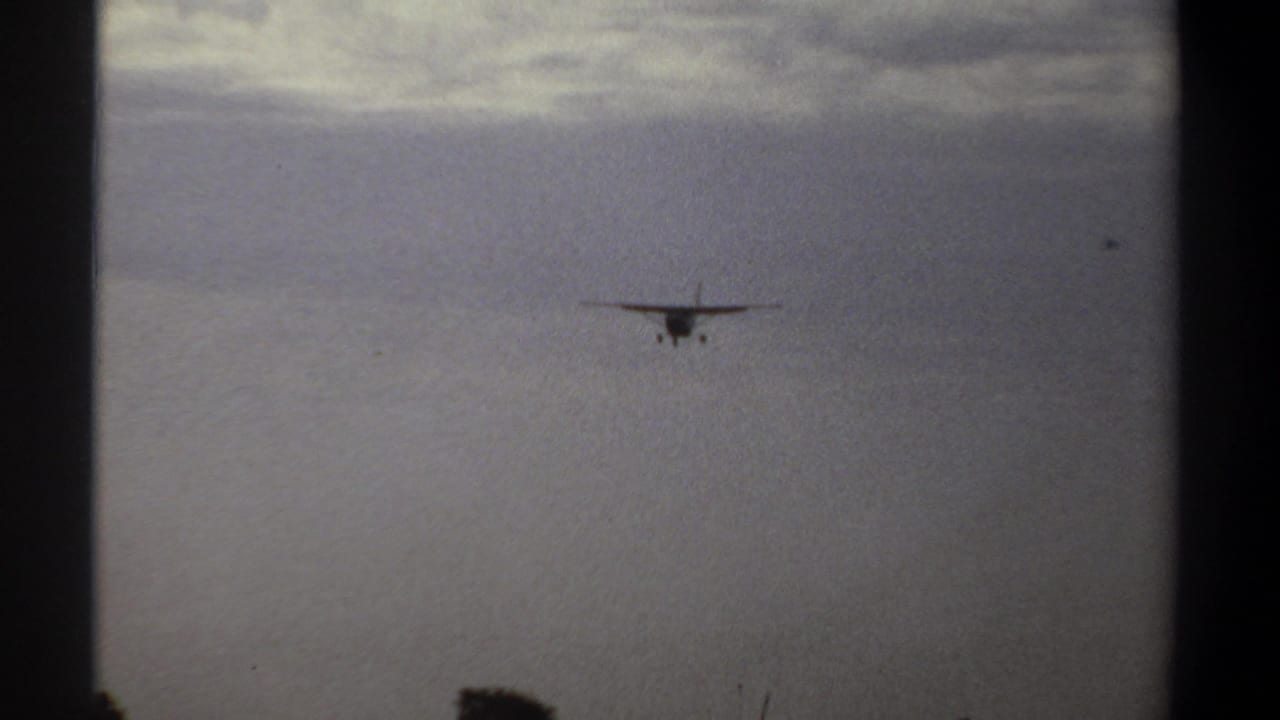 Small propeller airplane approaches over Khartoum, Sudan, in 1969 home-movie footage, seen distantly against a cloudy sky.