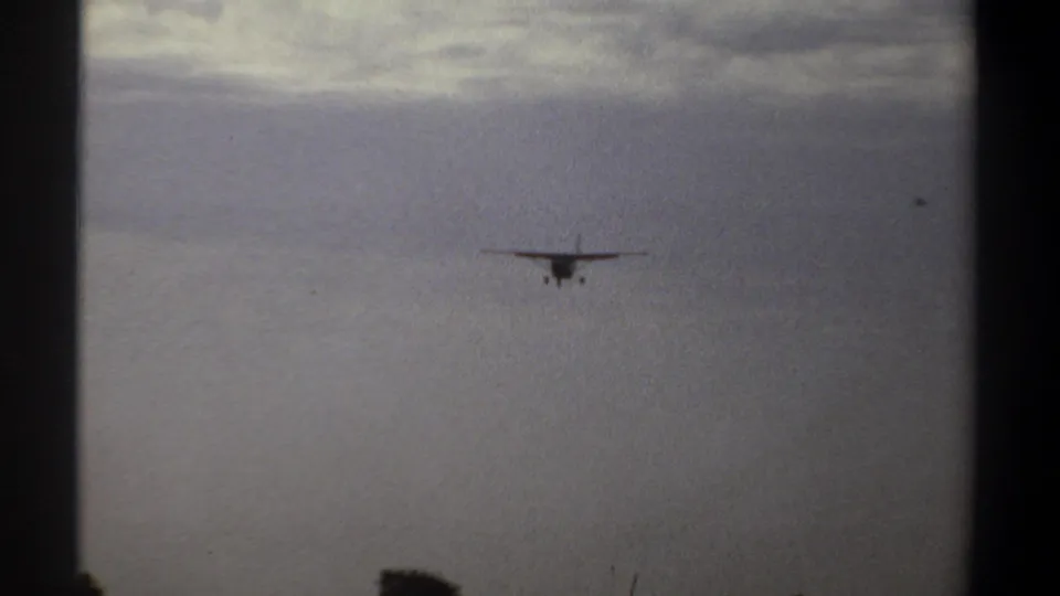 Small propeller airplane approaches over Khartoum, Sudan, in 1969 home-movie footage, seen distantly against a cloudy sky.
