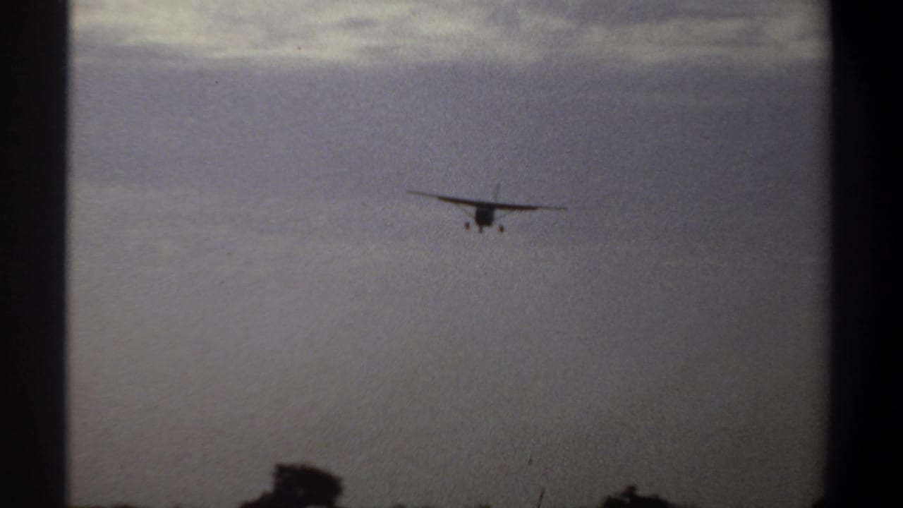 Distant airplane centered against gray clouds with landing gear visible.