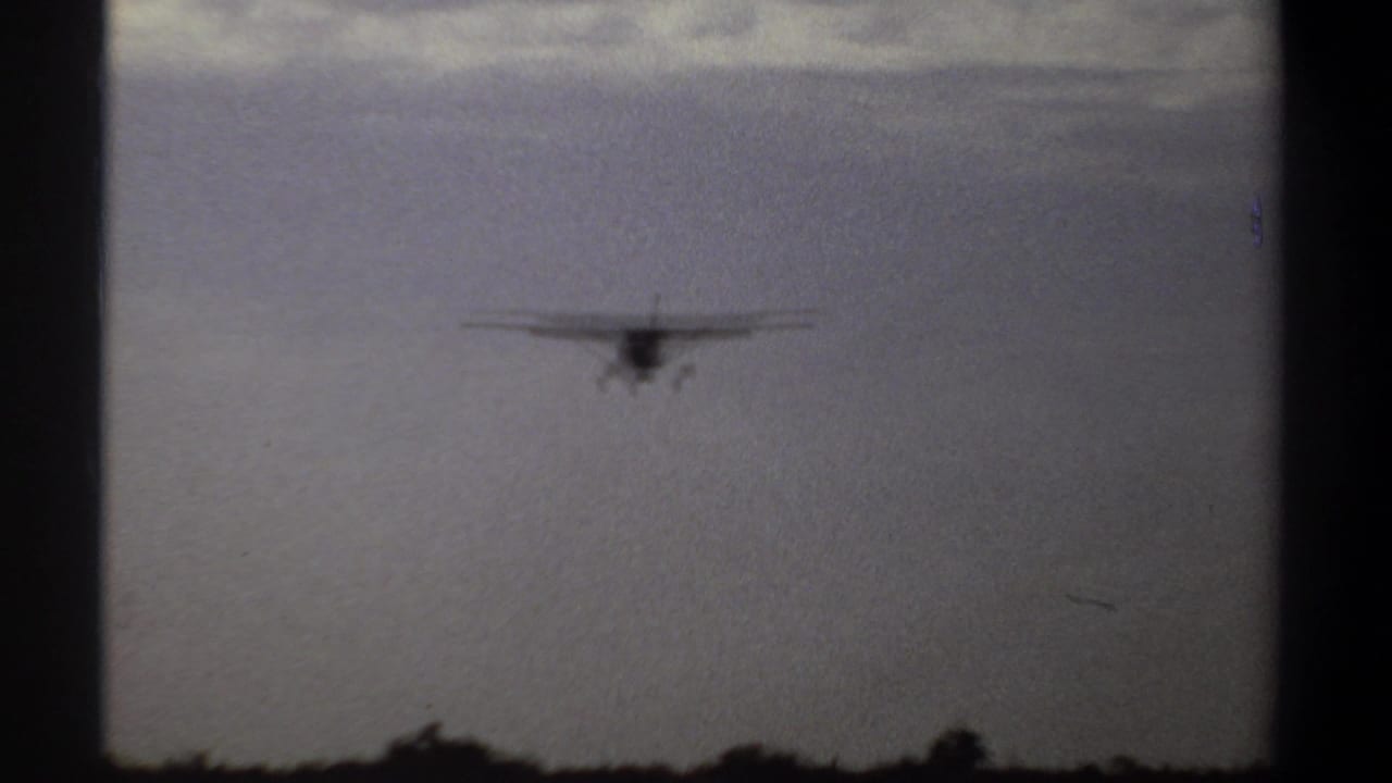 Small airplane silhouetted in a hazy sky above a low rural horizon.