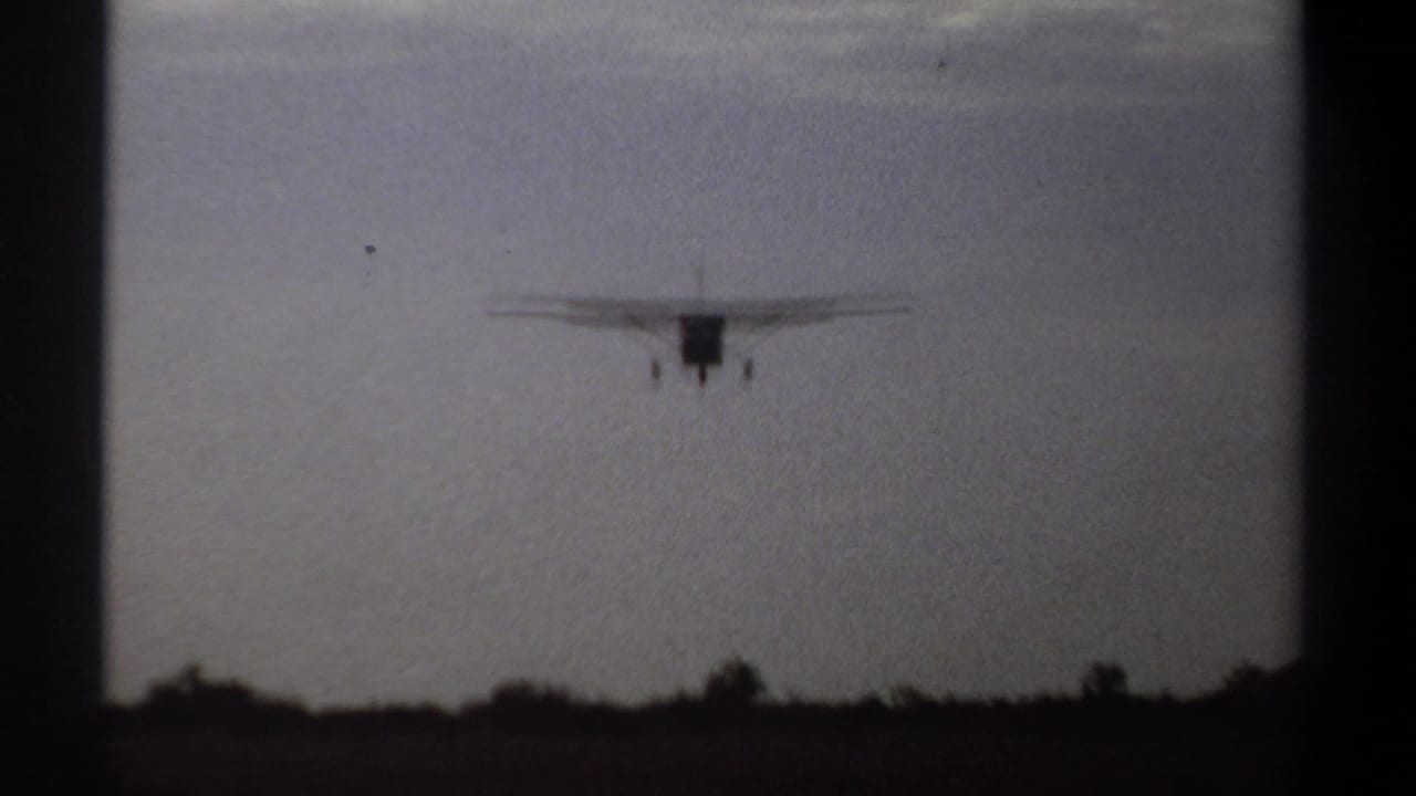 Small airplane descending with landing gear visible over a dark runway edge.