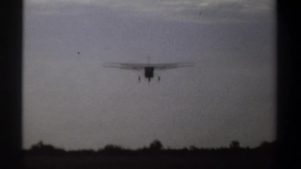 Silhouetted single-engine airplane descends toward a simple airstrip in 1969 Khartoum home-movie footage.
