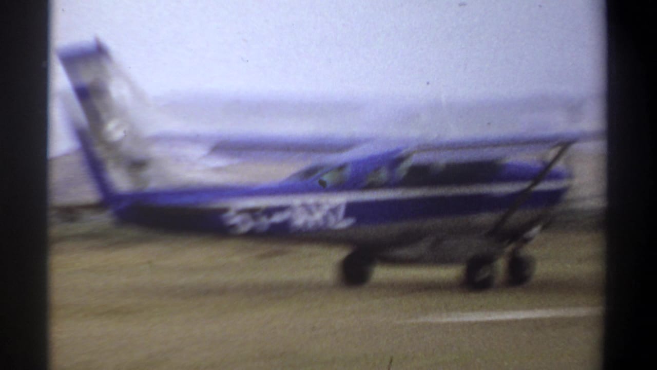 The high-wing aircraft rolls along the Khartoum grass airstrip, with white registration markings visible on its blue fuselage.