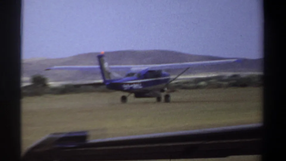 The blue and white aircraft appears low over or just above the Khartoum grass airstrip near the end of its takeoff run.