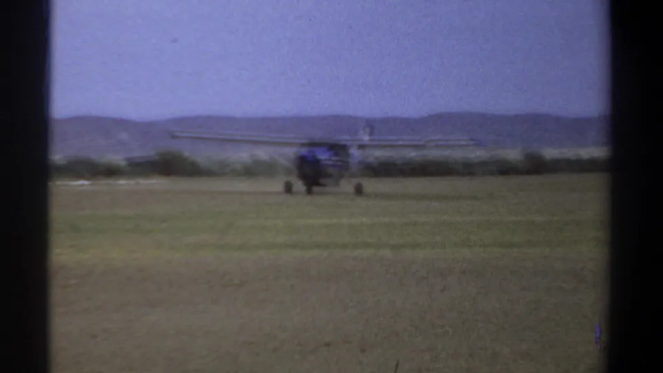 1969 Khartoum home-movie frame showing the front of a small aircraft on grass, with hills and a pale sky in the distance.