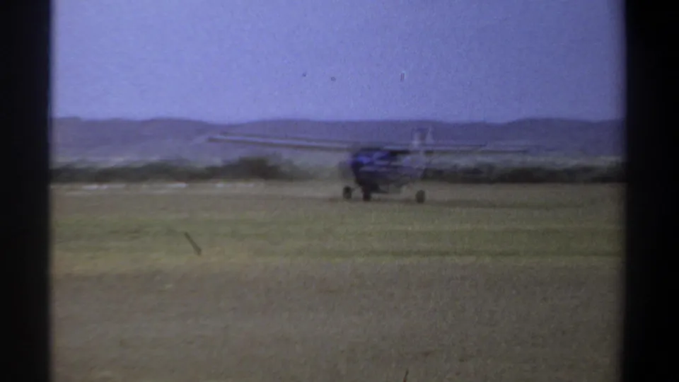1969 Khartoum frame showing a small airplane from the front on an open grass airfield with low hills behind it.