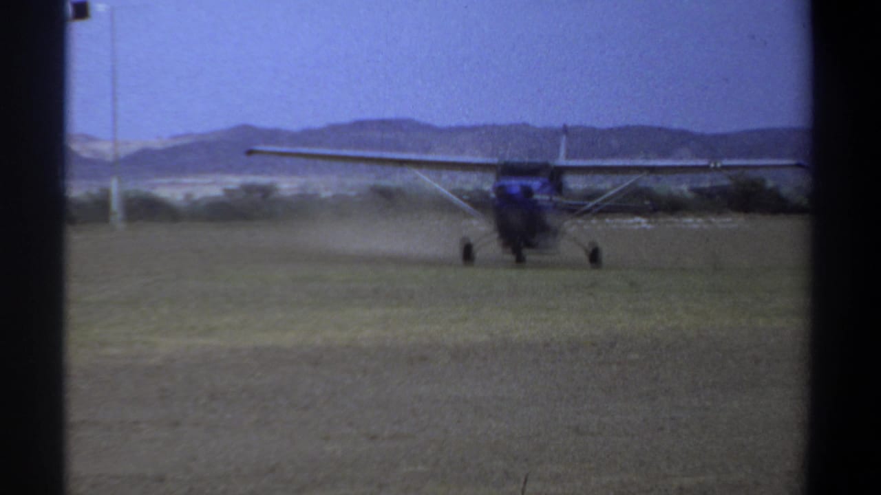 High-wing propeller airplane moving on grass with dust or blur near the runway.