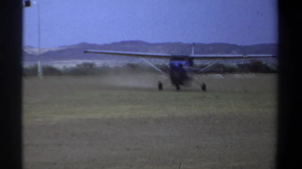 1969 Khartoum frame with a small single-engine airplane taxiing on a grass strip, viewed from the front against distant hills.