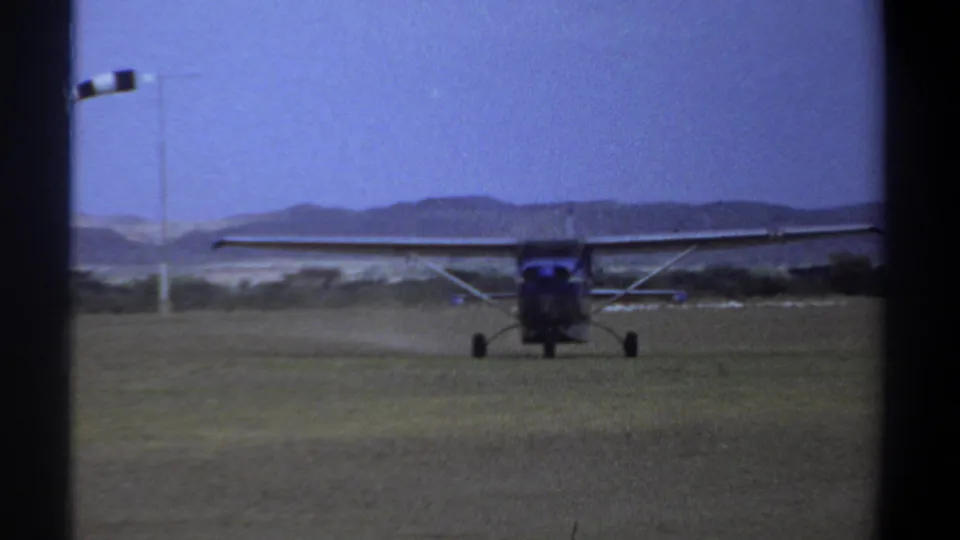 Front view of a small propeller airplane taxiing on a grassy Khartoum airfield in 1969, with hills and sky behind it.