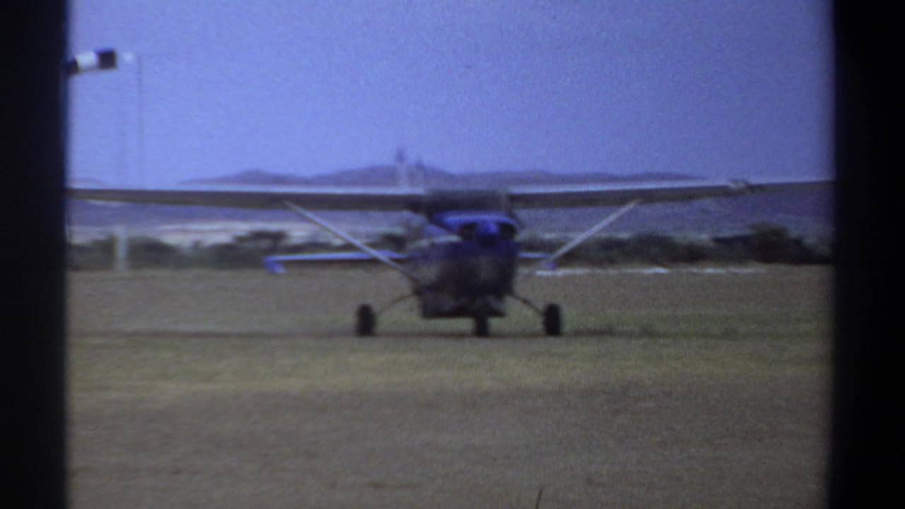 Small high-wing plane taxiing forward on grass with a windsock behind it.