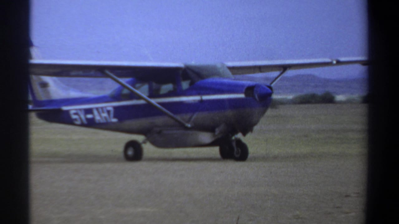 Side view of the blue and silver light aircraft on a Khartoum dirt runway, with partial registration lettering visible on the fuselage.