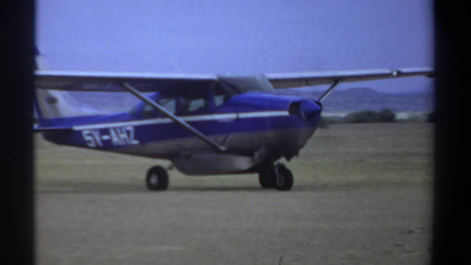 Side view of the blue and silver light aircraft on a Khartoum dirt runway, with partial registration lettering visible on the fuselage.