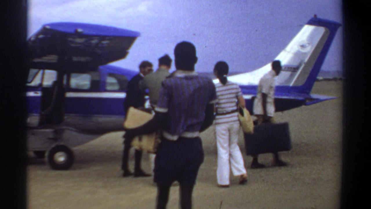 In 1969 Khartoum footage, several passengers carrying bags move toward a small blue and white aircraft on an open airfield.